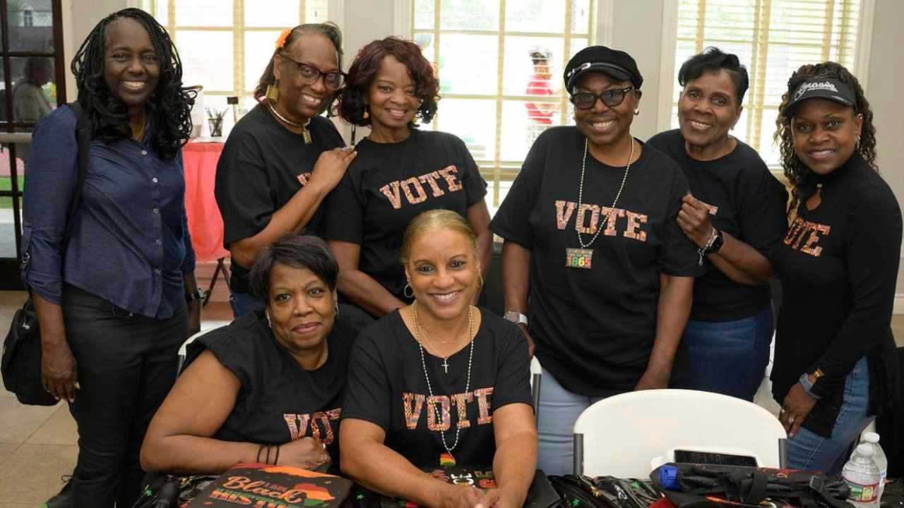 Group of people pose together indoors, many wearing matching “VOTE” shirts, gathered around a table at a Juneteenth-themed community event.
