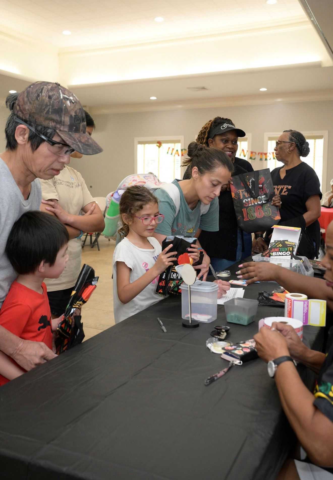 People line up at a table indoors during a Juneteenth event, collecting bags and tickets while volunteers distribute items and materials.