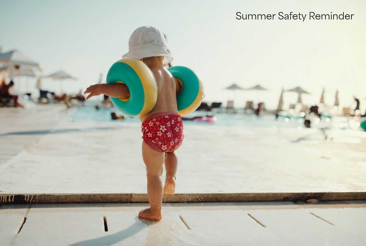 Child wearing a sun hat and colorful arm floaties walks toward a swimming pool on a sunny day. Text in upper right reads, “Summer Safety Reminder.”